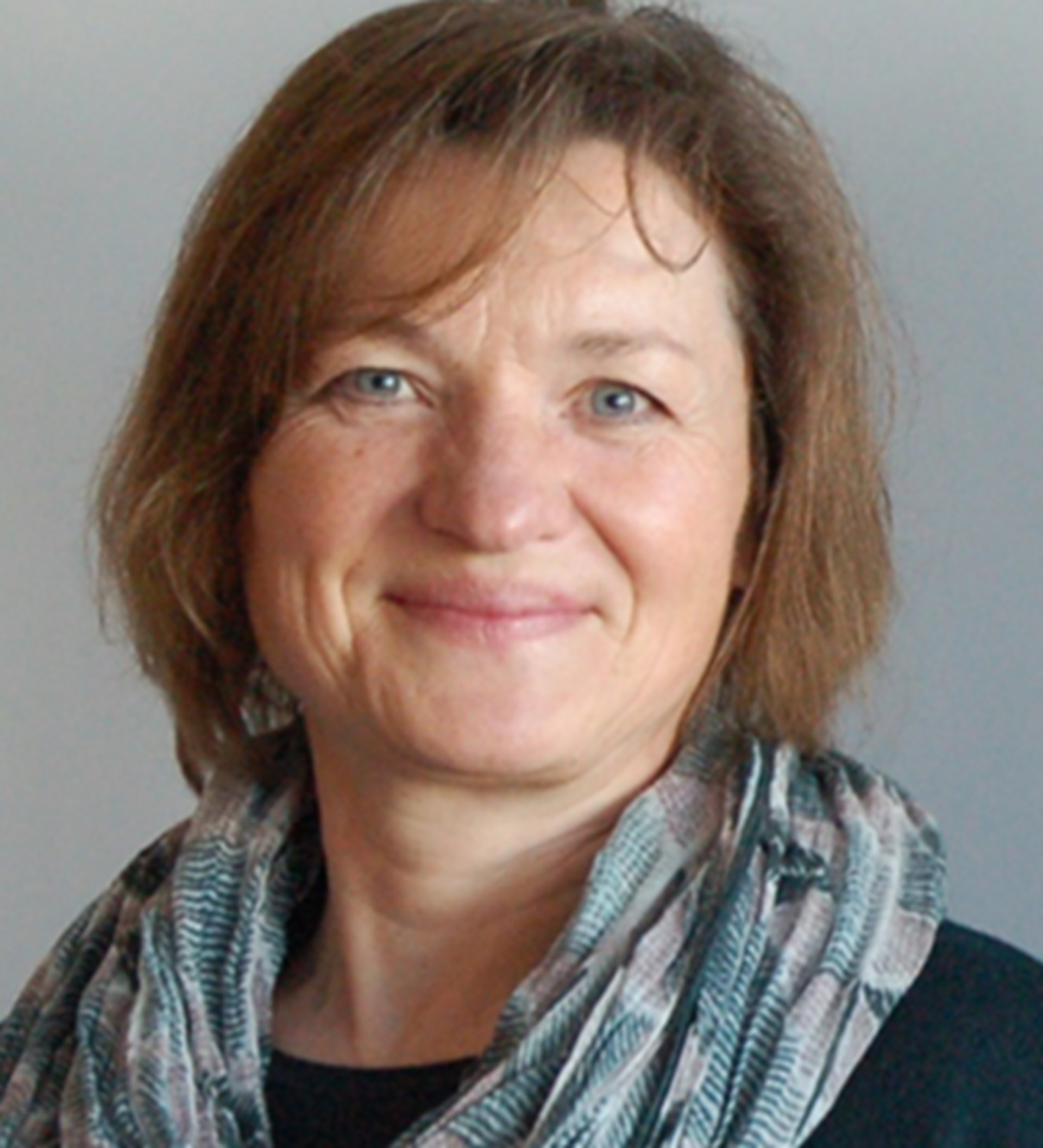 Lächelnde Frau mit schulterlangen braunen Haaren, Schal und schwarzem Oberteil.