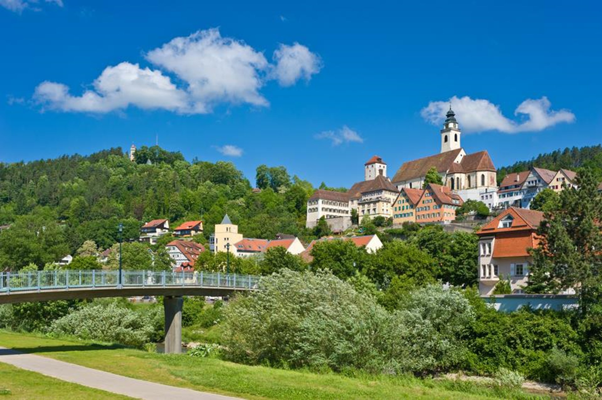 Malerische Stadtansicht mit Brücke, grüner Landschaft und blauem Himmel.