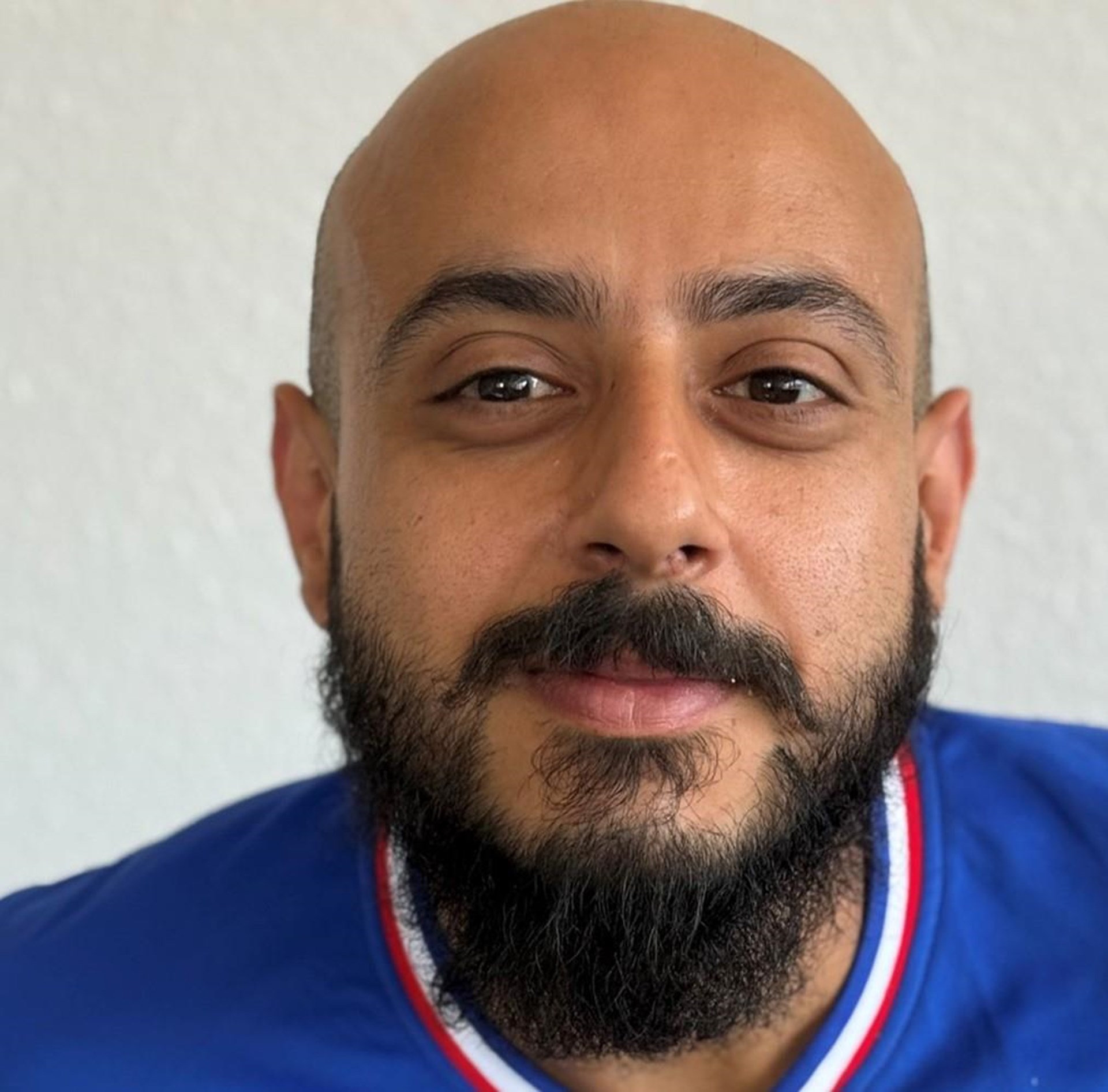 Porträt eines bärtigen Mannes mit Glatze und blauem Shirt vor hellem Hintergrund